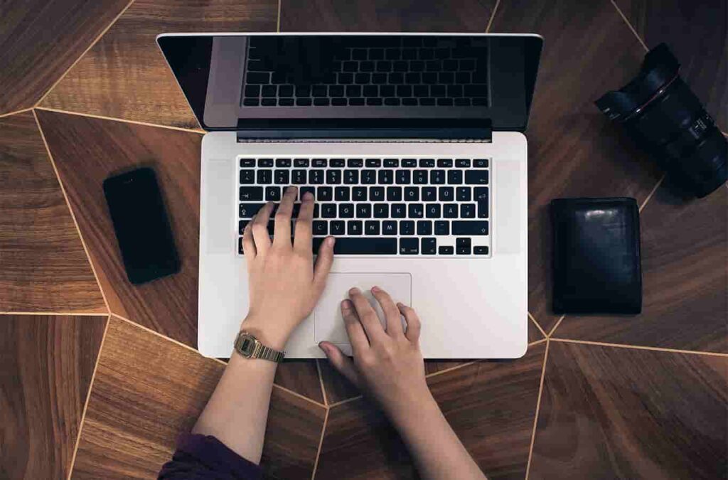 Aplikasi Berbasis Web: Pengertian, Jenis, Contoh, & Manfaat Seseorang sedang mengetik mengunakan laptop.