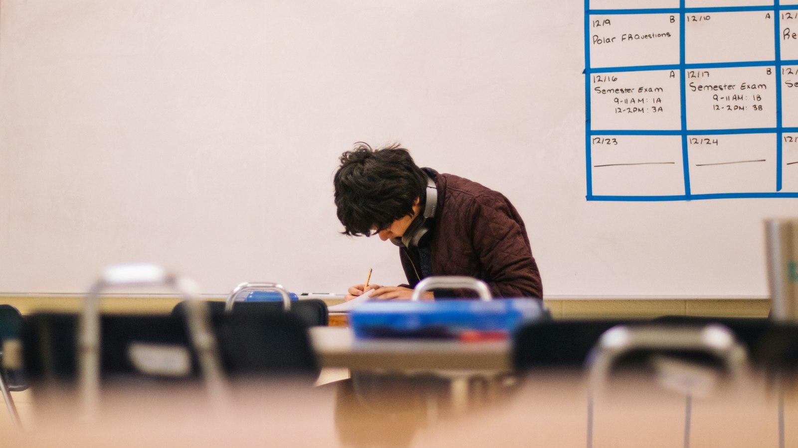 Asesmen Formatif, Sumatif, dan Cara Mengolah Nilai Rapor Kurikulum Merdeka Murid menulis di meja kelas dengan jadwal ujian semester di papan tulis