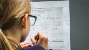 Murid berkacamata mengerjakan lembar soal dengan pensil