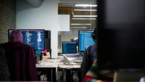 Programmer bekerja di depan monitor berisi kode di ruang kerja