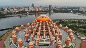 Tampak udara masjid berkubah jingga di tepi perairan dengan latar kota