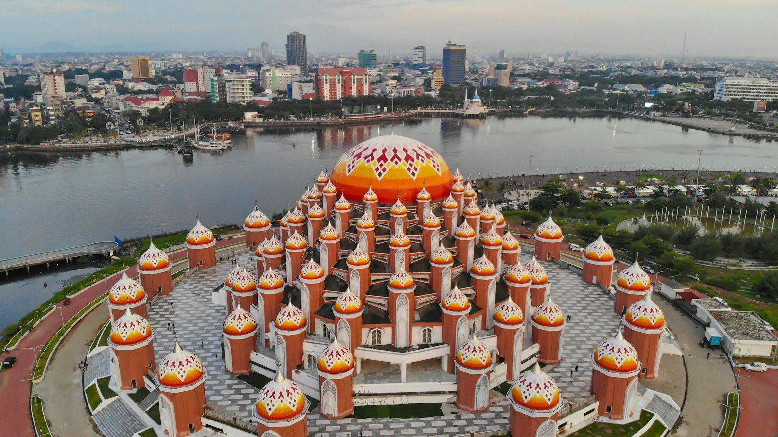 Tampak udara masjid berkubah jingga di tepi perairan dengan latar kota