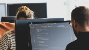 Dua programmer bekerja di depan monitor yang menampilkan kode program