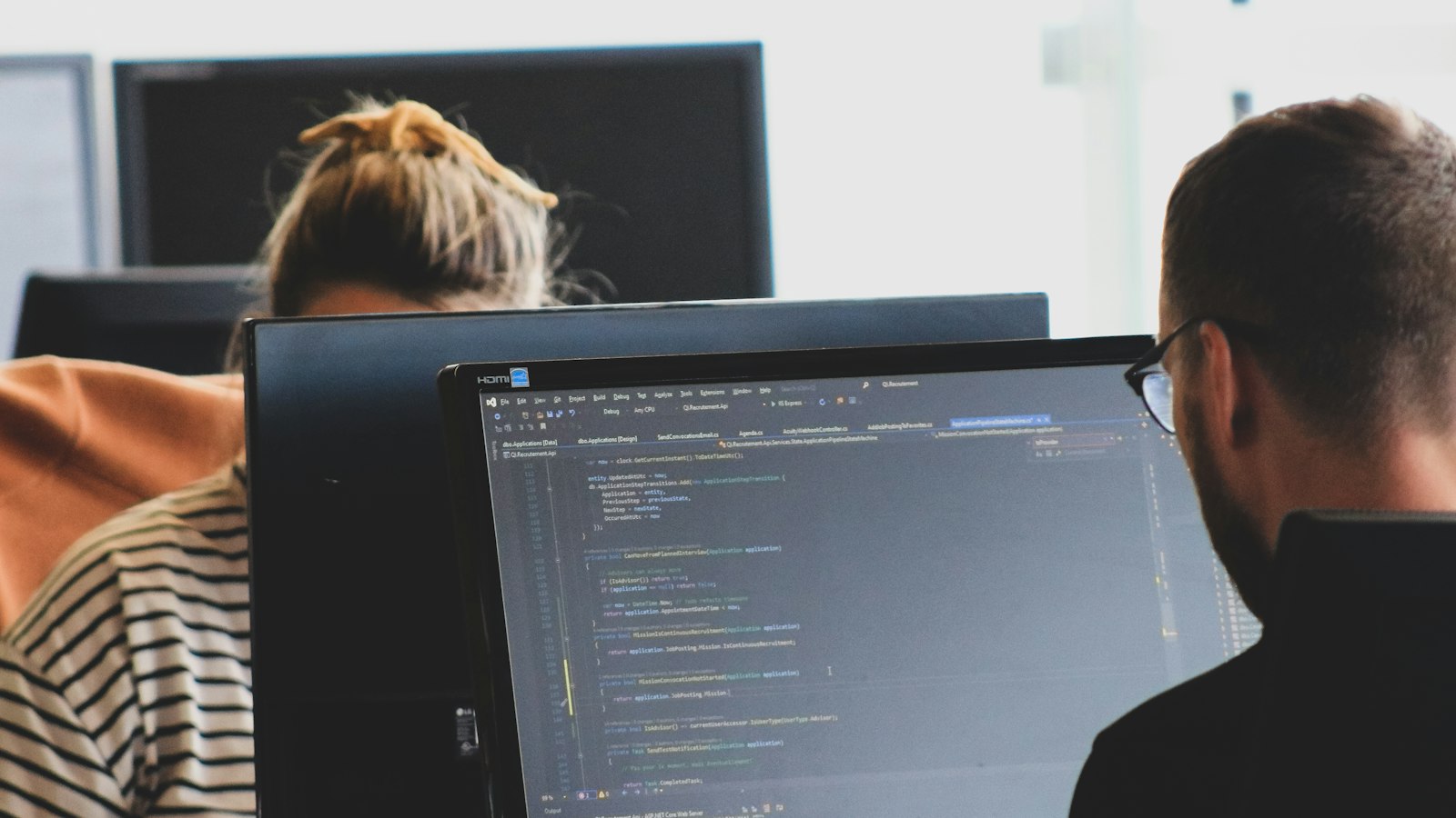Dua programmer bekerja di depan monitor yang menampilkan kode program
